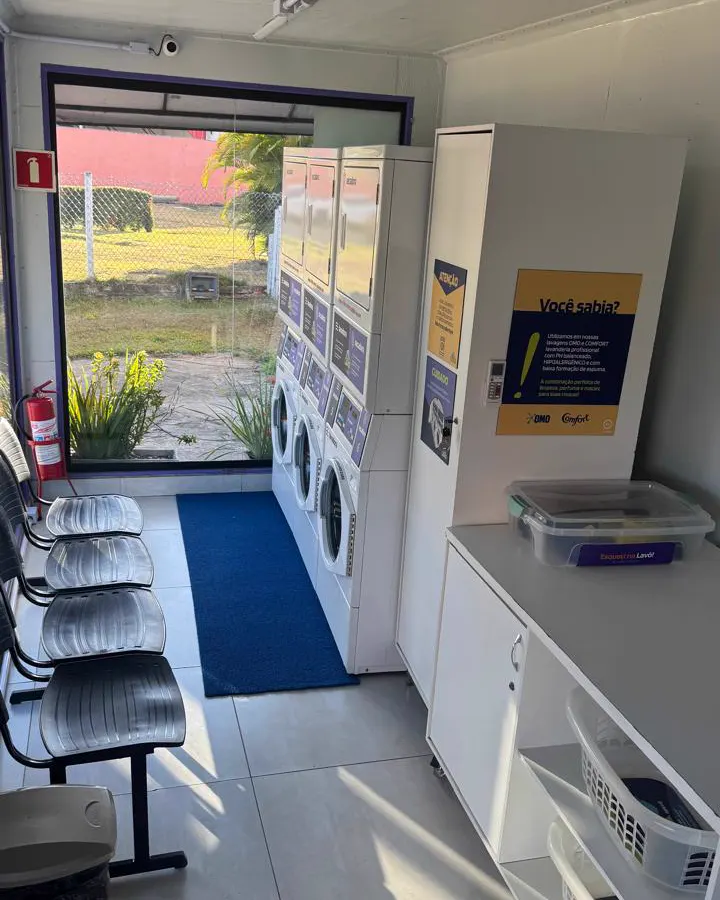 Interior da Lavô Busca Vida com os três conjuntos de lavadora e secadora, bancos de espera e bancada